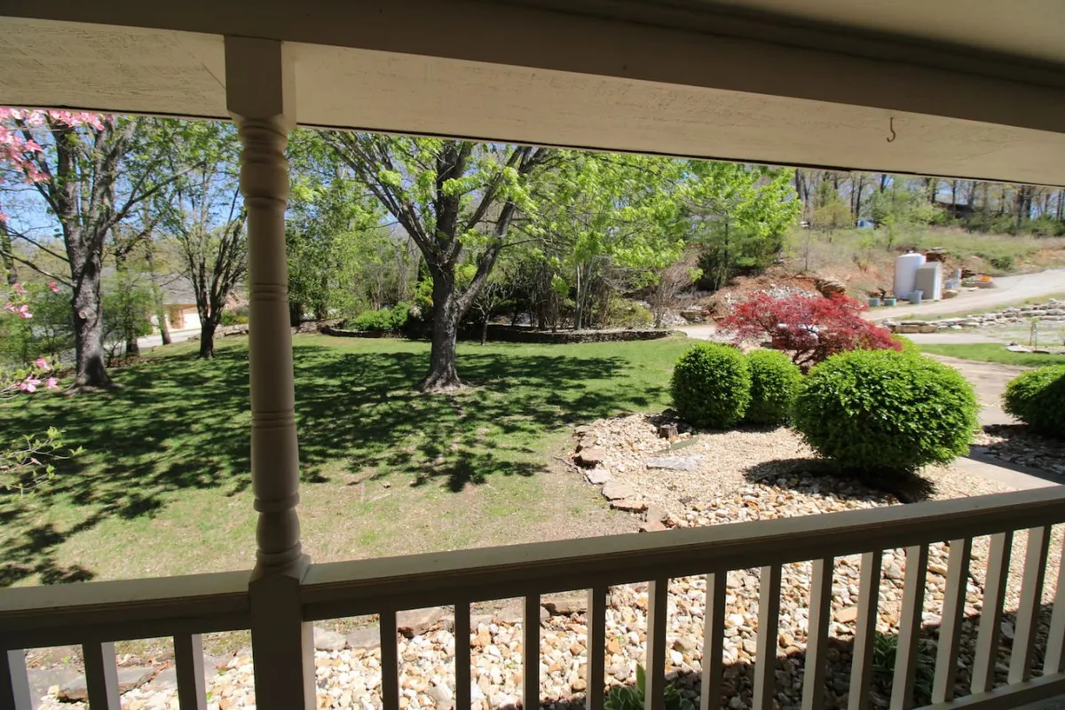 This image captures a lush green lawn bordered by flowering trees and features a decorative stone pathway leading toward the porch. The inviting exterior setting hints at ample space for outdoor relaxation and gatherings, with nature providing a tranquil backdrop.