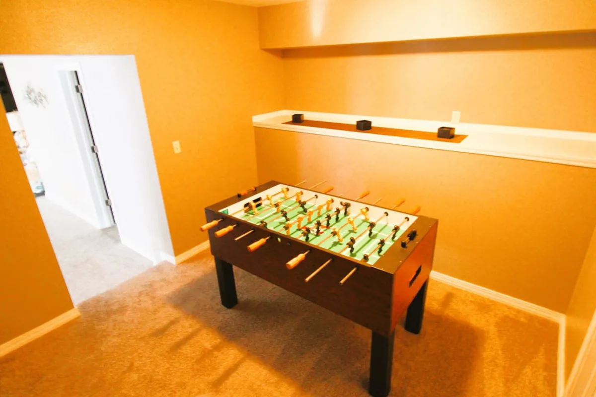A foosball table sits at the forefront of a stylish game room, with an open doorway leading to another part of the house. The space feels casual and inviting—perfect for friendly competition and group interaction, with plenty of space to move around.