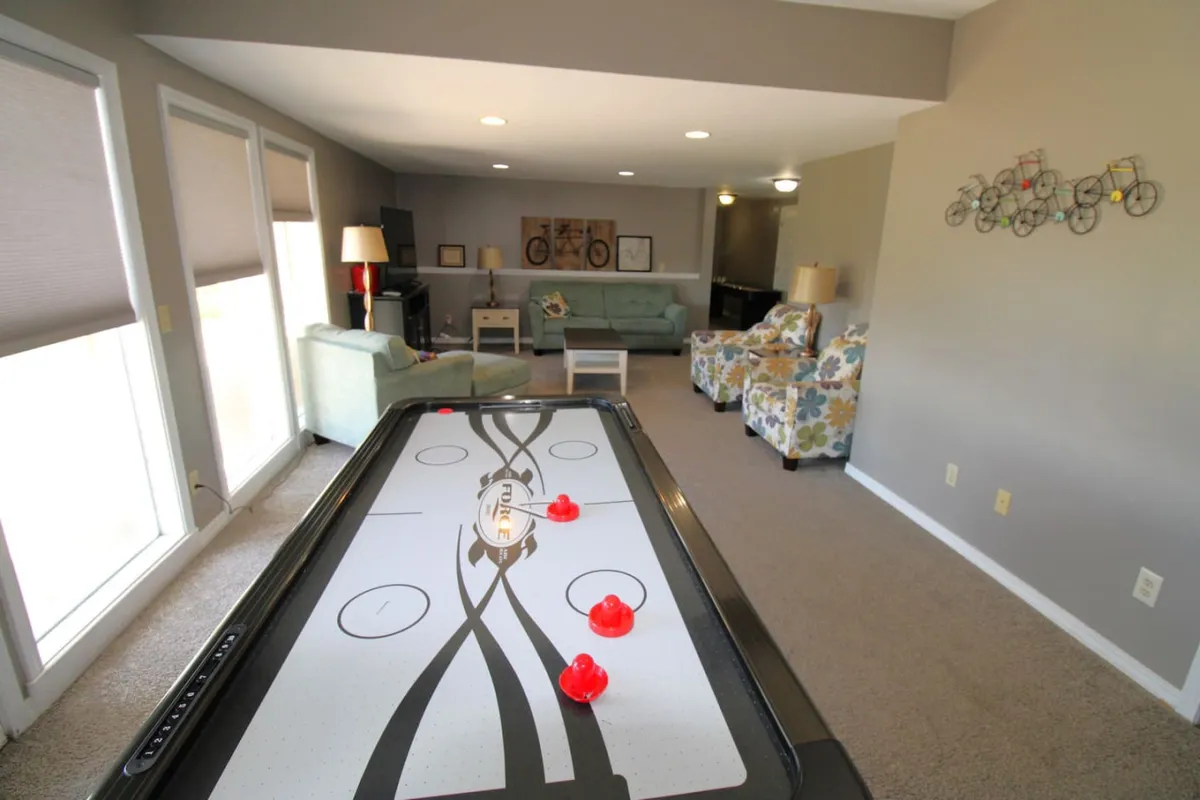 A colorful, inviting scene featuring an air hockey table, floral-patterned chairs, and a cozy sofa set. The room is designed for both spirited competition and relaxing moments, ideal for groups of all ages.