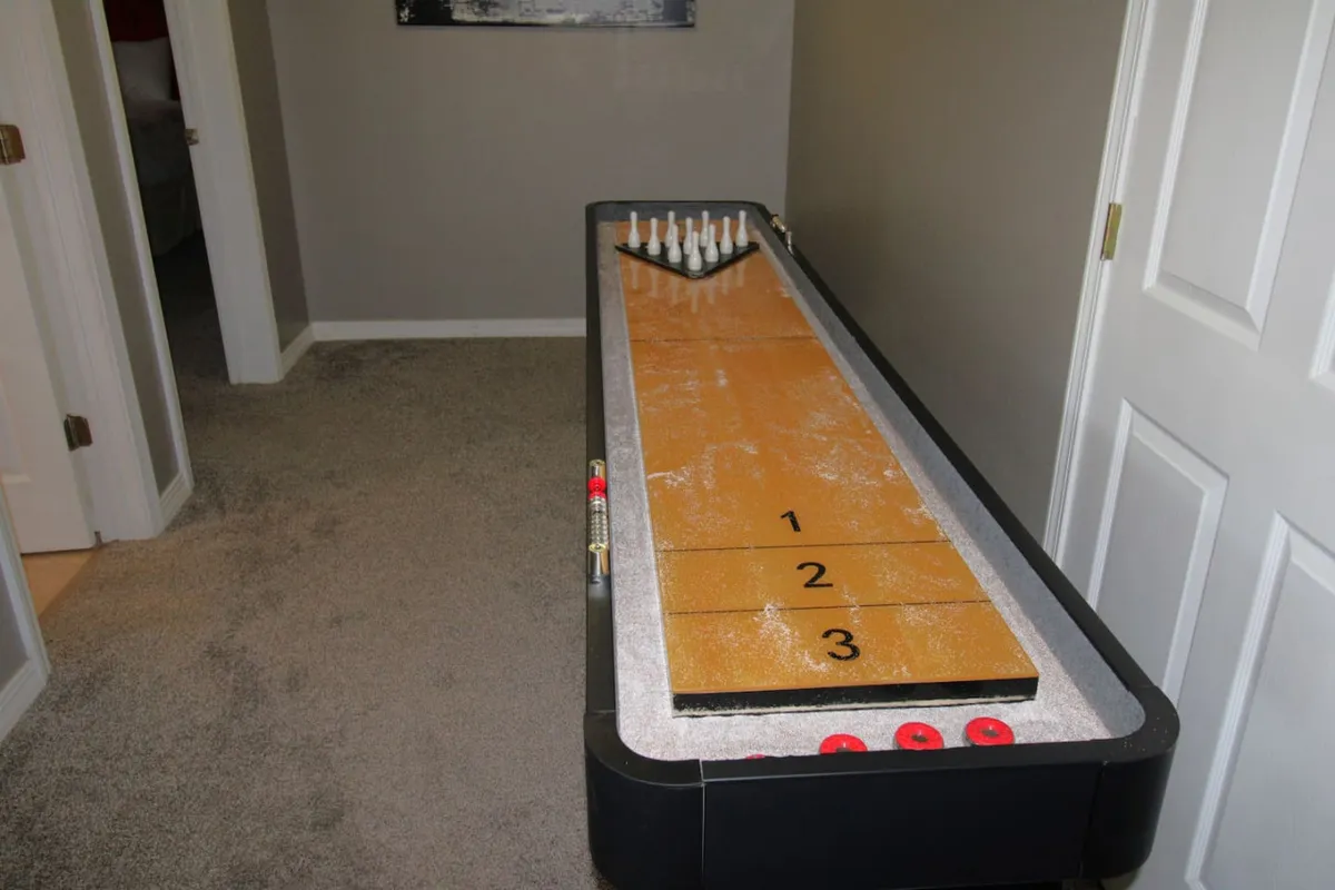 An interior shot of a lively game space featuring a shuffleboard table, bowling pins, and a scoring area. The playful decor and setup suggest active fun and friendly competition, ideal for families or groups.