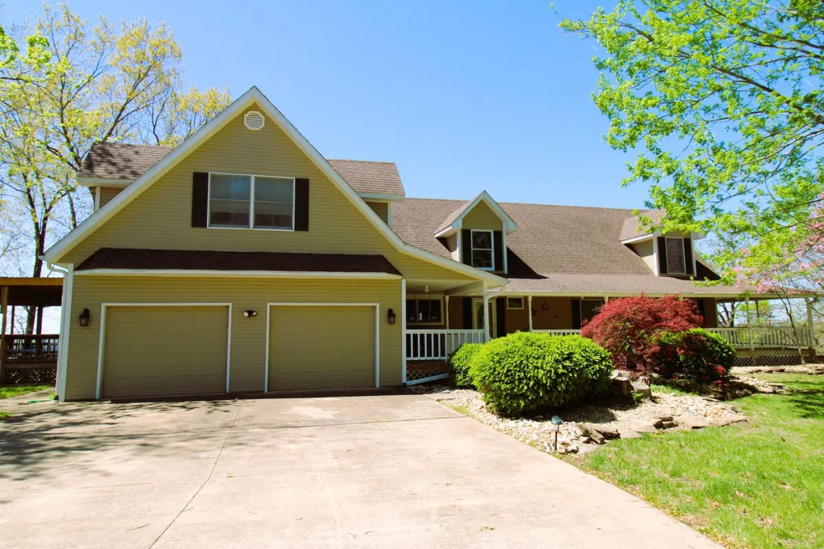 The home’s inviting exterior features a wrap-around front porch, a manicured lawn, decorative shrubbery, and a two-car garage—a perfect space for gatherings and relaxing after a day on the lake.