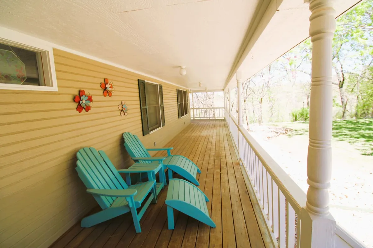 This image captures a welcoming exterior scene featuring turquoise Adirondack chairs arranged on a wooden deck, colorful wall decorations, and a sturdy wooden railing. The setup invites socializing and relaxation while enjoying the fresh air and the property's surroundings.