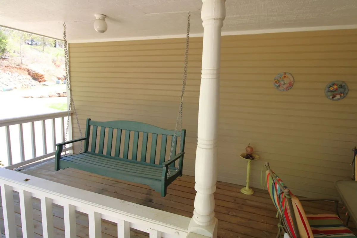 Showcasing a swing bench, decorative plates, and a colorful chair, this porch scene radiates warmth and relaxation. The setup invites guests to gather for quiet moments, casual conversations, or simply to watch the sunset and enjoy nature's tranquility.