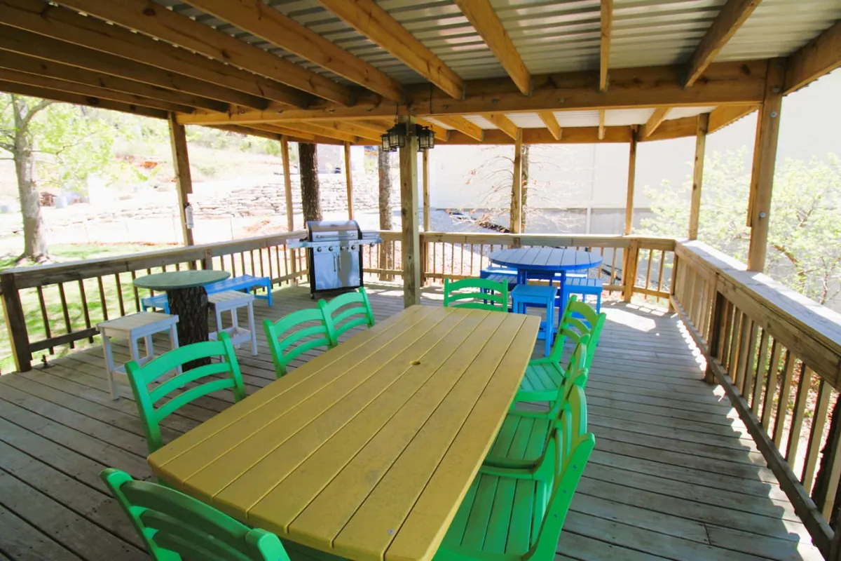 A vibrant exterior shot of a porch area with a large yellow table, cheerful chairs, a grill, and lush greenery all around. The setting is clearly prepared for outdoor dining and lively gatherings, embodying the entertainer's dream described in the section.