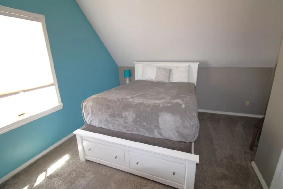 A serene bedroom interior featuring a cozy bed against a blue accent wall, with a nightstand and lamp providing a soft, restful glow. The mood is calm and peaceful, ideal for an adult retreat after a busy day. The soft light and uncluttered space evoke a sense of luxury and privacy.