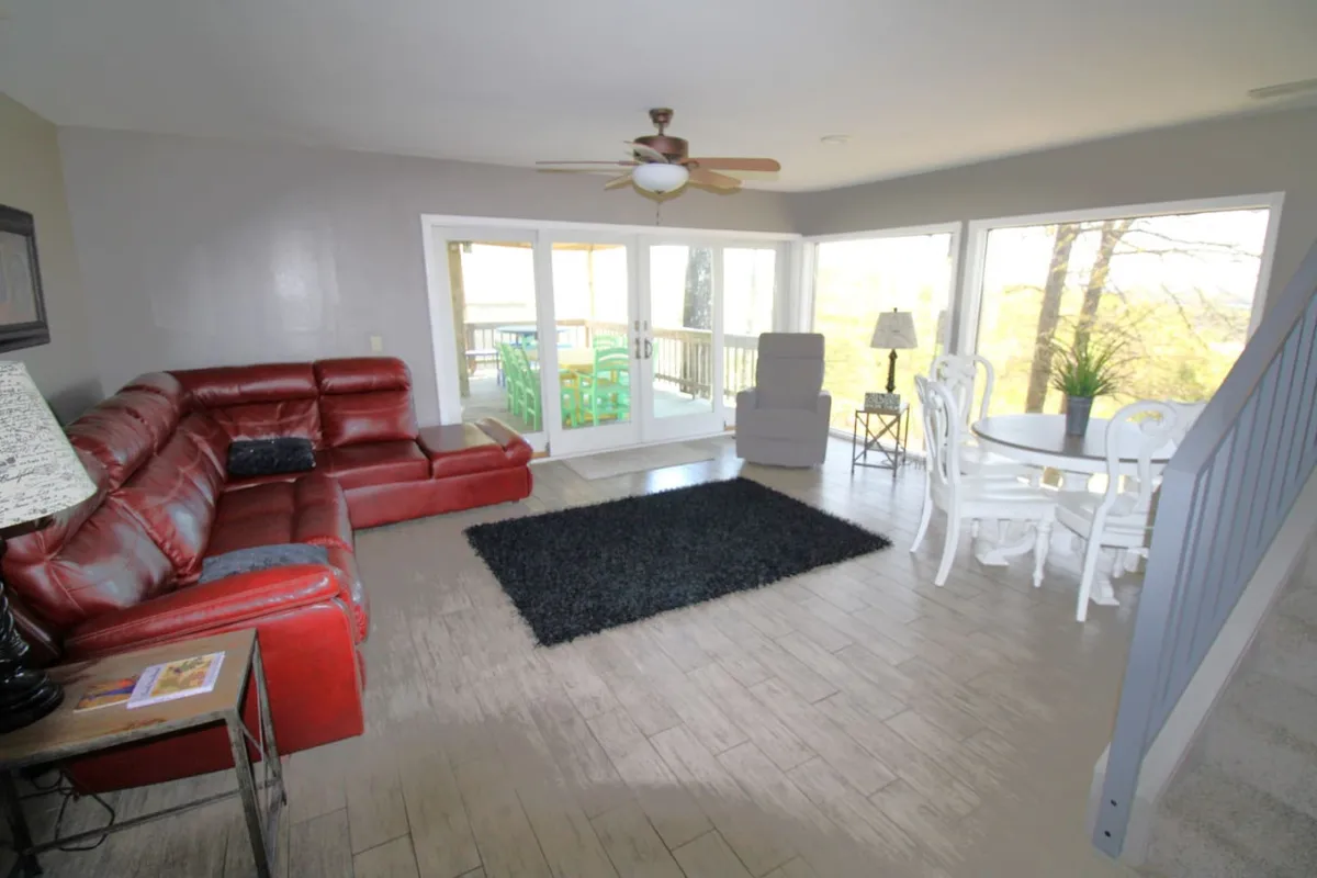 This image features an inviting interior gathering space with a red sectional sofa, a white dining set, and large windows that showcase beautiful views of the outdoors. The space is bathed in natural light, making it ideal for group activities, relaxation, and shared meals.