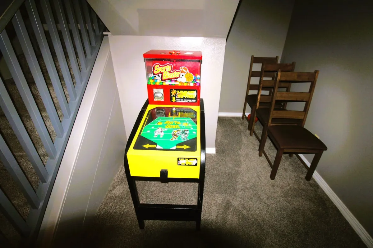 A close-up of an arcade game machine accompanied by wooden chairs, reflecting a cozy yet playful atmosphere where guests can engage in friendly arcade competitions.
